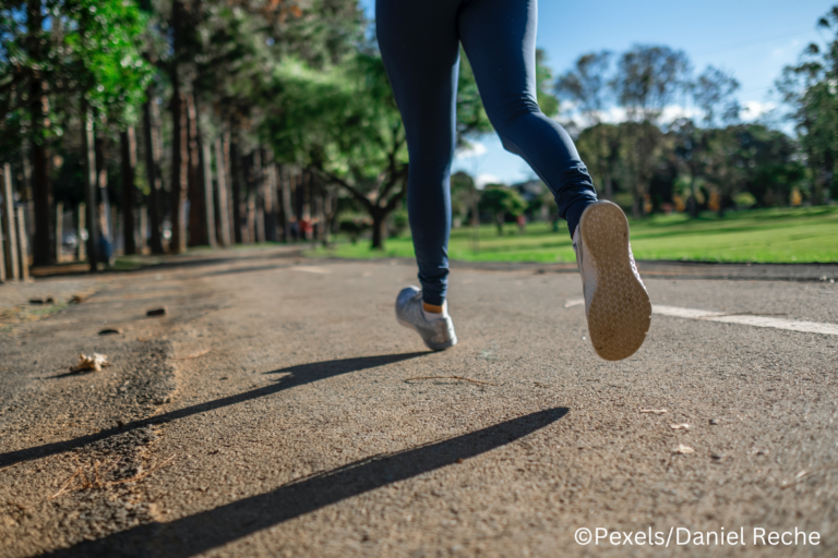 Eine laufende Person, von der nur die Beine zu sehen sind, die auf einer Straße in einem grünen Park läuft